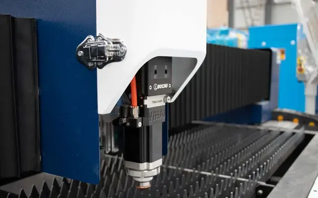 A CNC laser head cutting a sheet of metal on a workshop bed