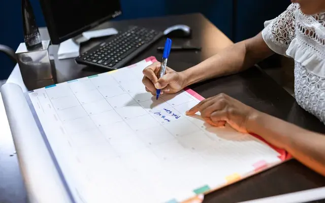 Hands marking a date in a paper planner with a red pen