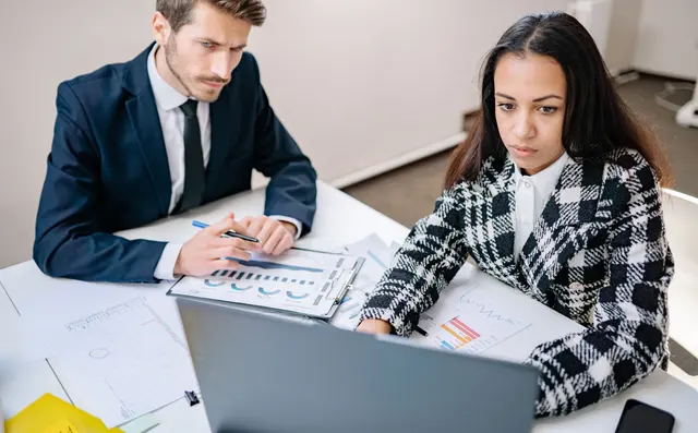 Two consultants reviewing figures on paper and a laptop