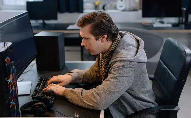 A developer writing code at a workstation in an open office