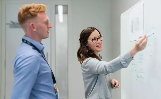 Two engineers discussing a diagram at a whiteboard