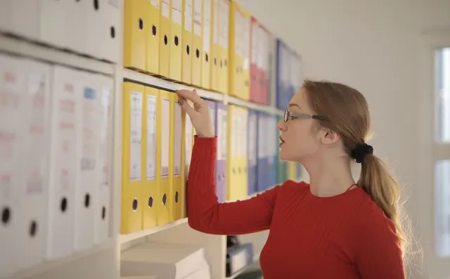 A worker searching binders on an archive shelf