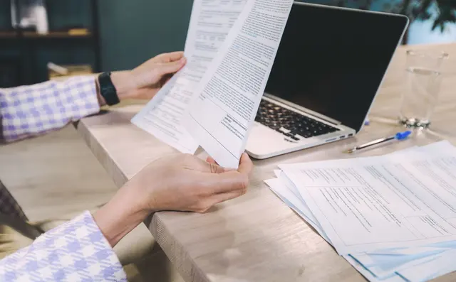 A finance manager working late with printed reports and a laptop