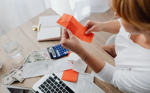 Hands sorting supplier invoices with a calculator