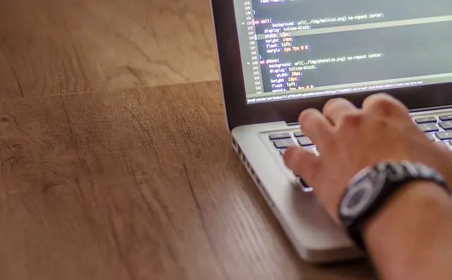 Hands on a laptop keyboard with code on the screen