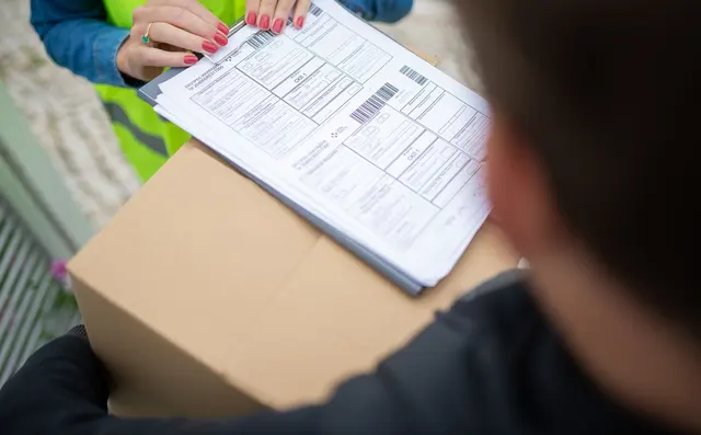 A driver signing off a consignment note beside a parcel