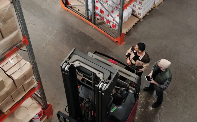 Two staff conferring beside a forklift, one holding a tablet